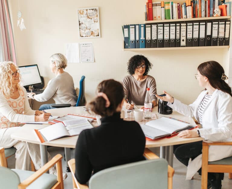 887A1411-Bearbeitet Mehrere Mitarbeiterinnen sitzen mit einer Ärztin am Besprechungstisch zum Meeting.