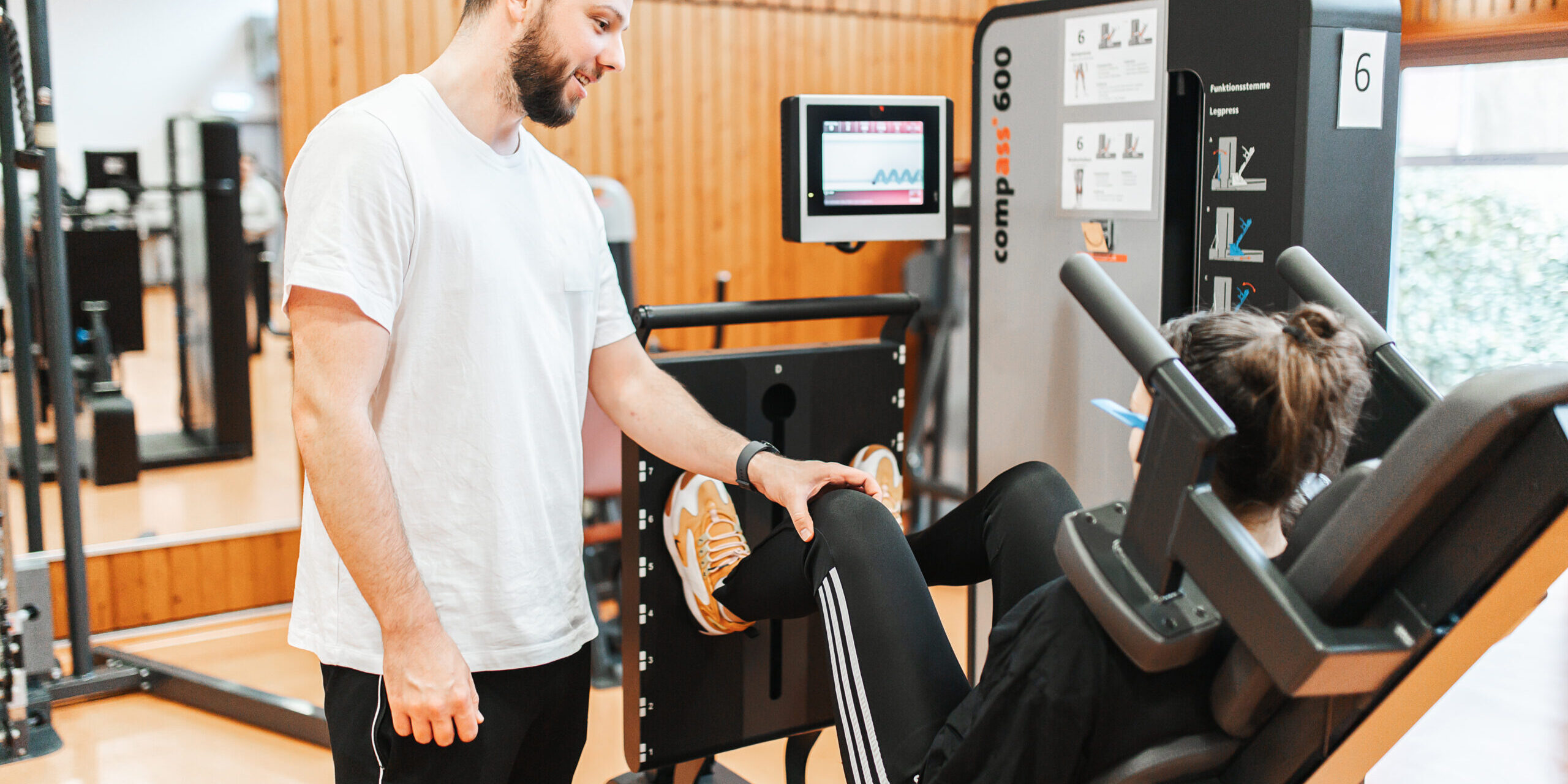 887A7677-Bearbeitet Ein Physiotherapeut betreut eine Patientin auf dem Fitnessgerät.
